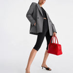A model poses in a gray double-breasted blazer, black cropped leggings, and black slide sandals, holding a bright red structured handbag against a clean white studio background.