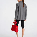 A woman shown from the back wearing a gray blazer, black cropped leggings, and black heeled mules, while holding a bright red structured handbag against a clean white studio background.