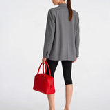 A woman shown from the back wearing a gray blazer, black cropped leggings, and black heeled mules, while holding a bright red structured handbag against a clean white studio background.