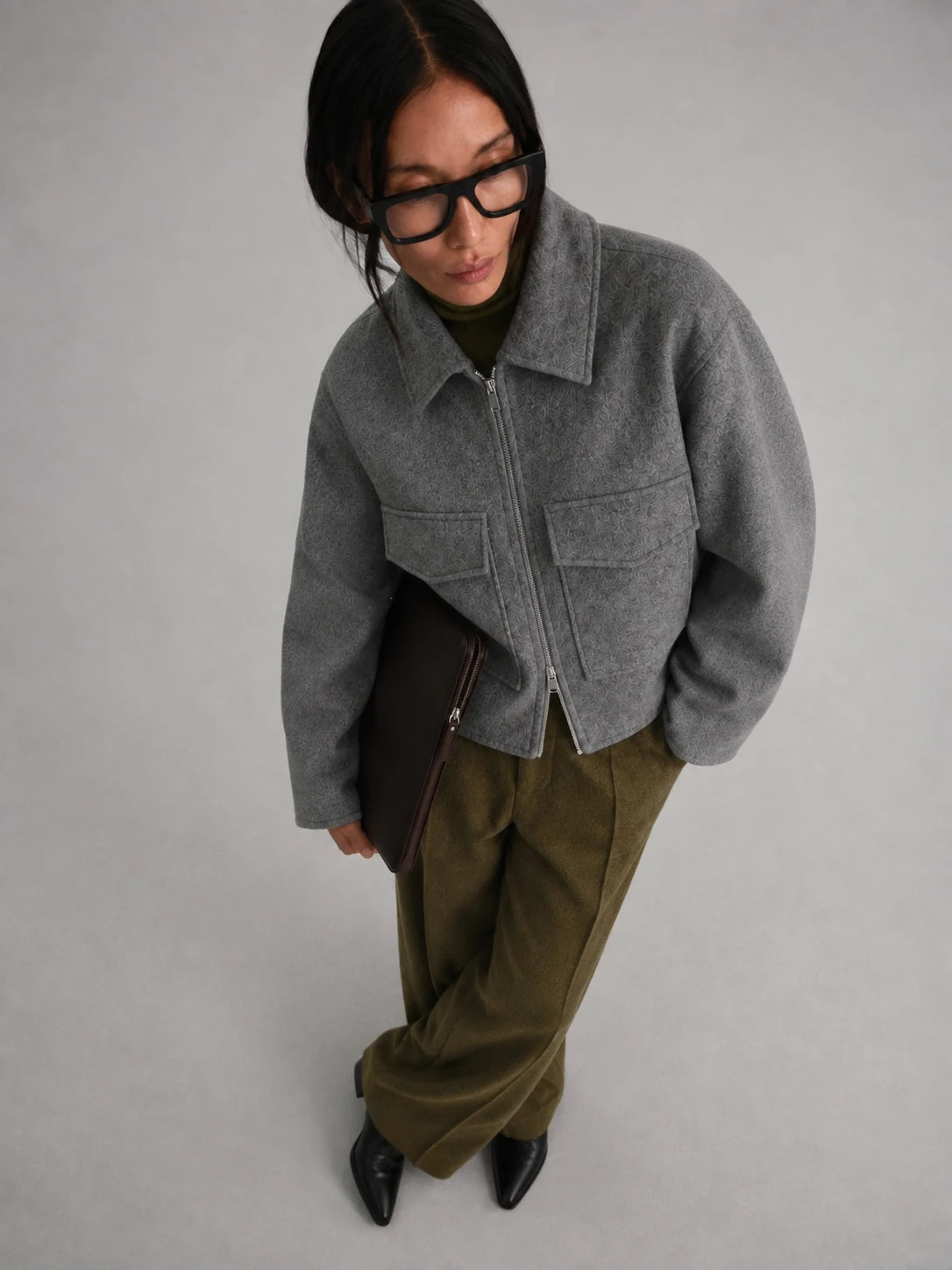 women is earing a Short Tweed Coat in grey with green trousers, black shoes and glases