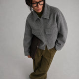 women is earing a Short Tweed Coat in grey with green trousers, black shoes and glases
