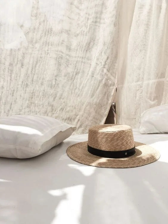 FERNACHE straw hat on white linen bedding – elegant summer accessory inspired by Old Money coastal style.