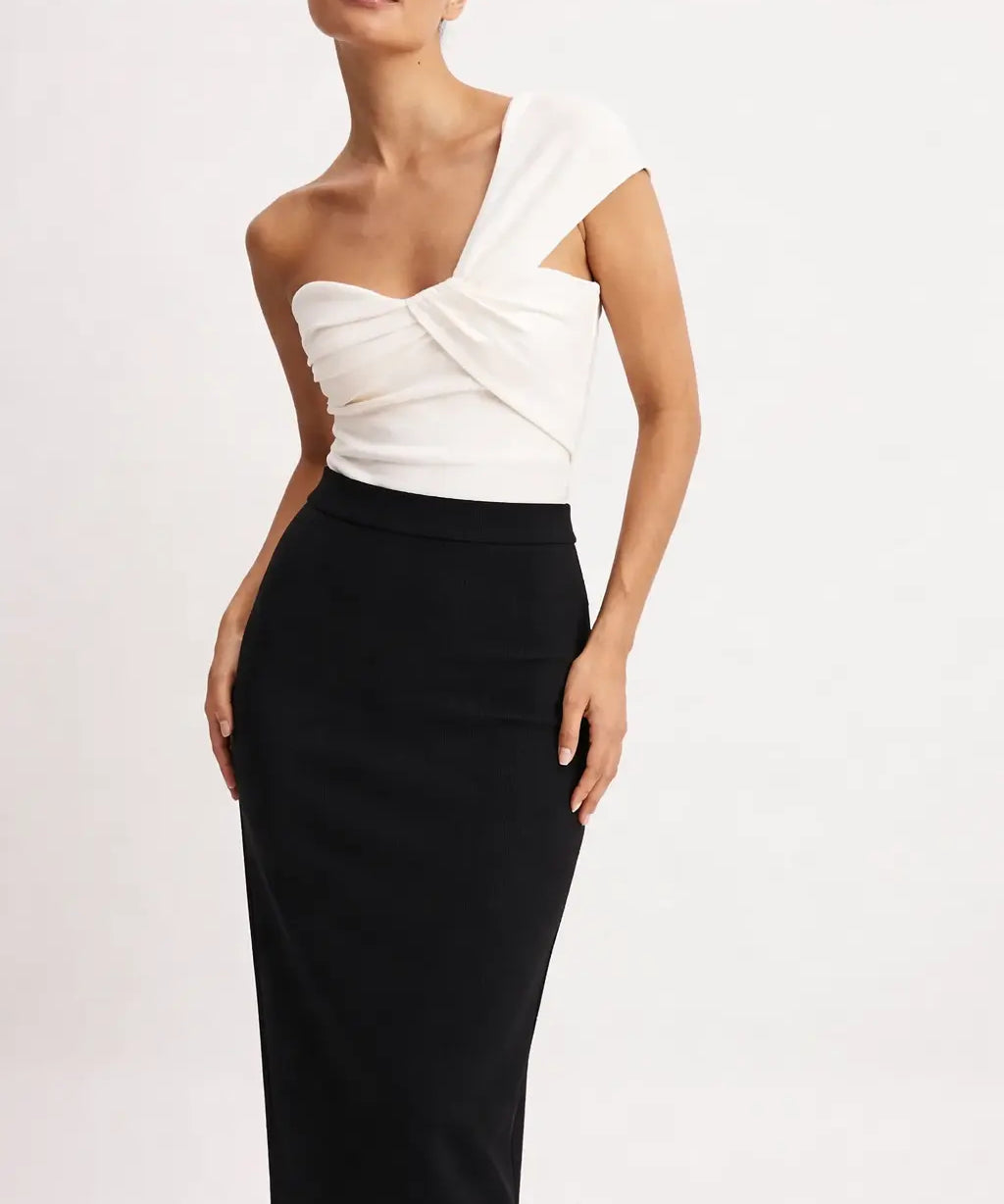 Woman wearing a white one-shoulder top and black pencil skirt on a light pink background